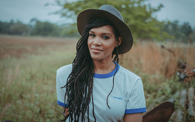 Contributing writer for this article, Candace Dantes, poses in a field wearing a gray hat.